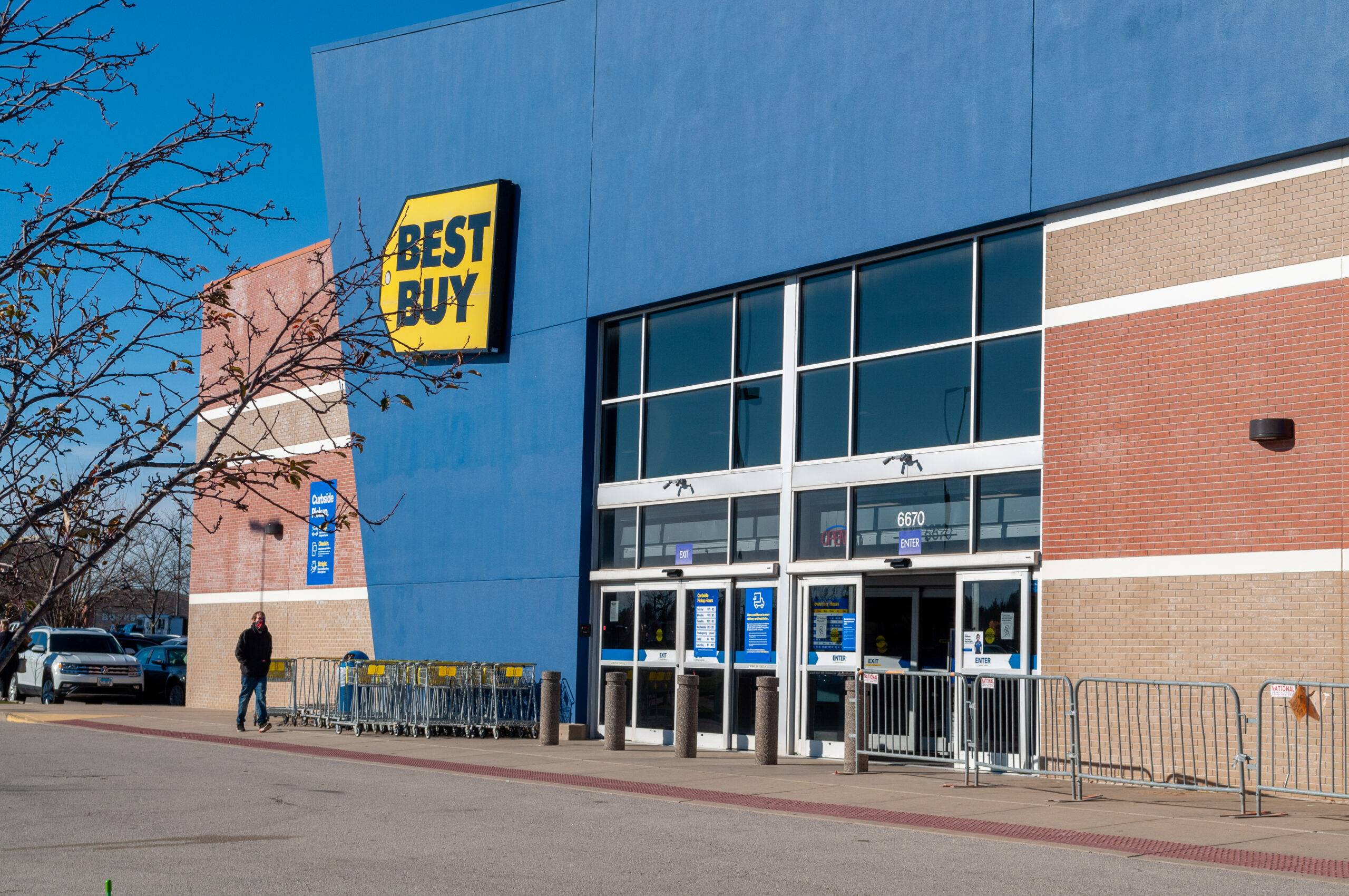 Best Buy store with gates set up to organize Black Friday shoppers. The gates are empty and a lone person stands outside the store.