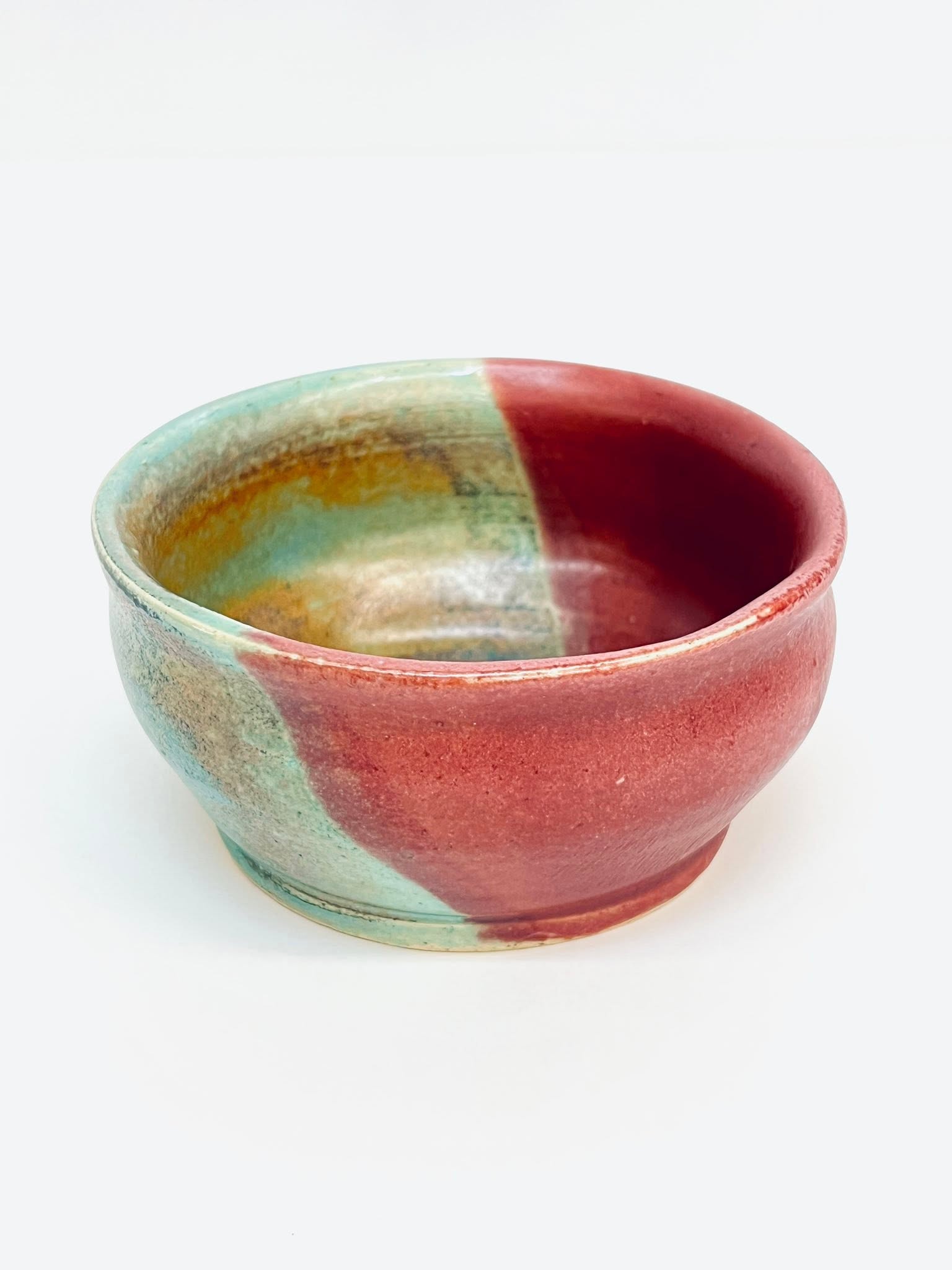 A handmade ceramic bowl with a split-color glaze, featuring a deep reddish-pink on one side and a textured, seafoam green and earthy brown on the other.